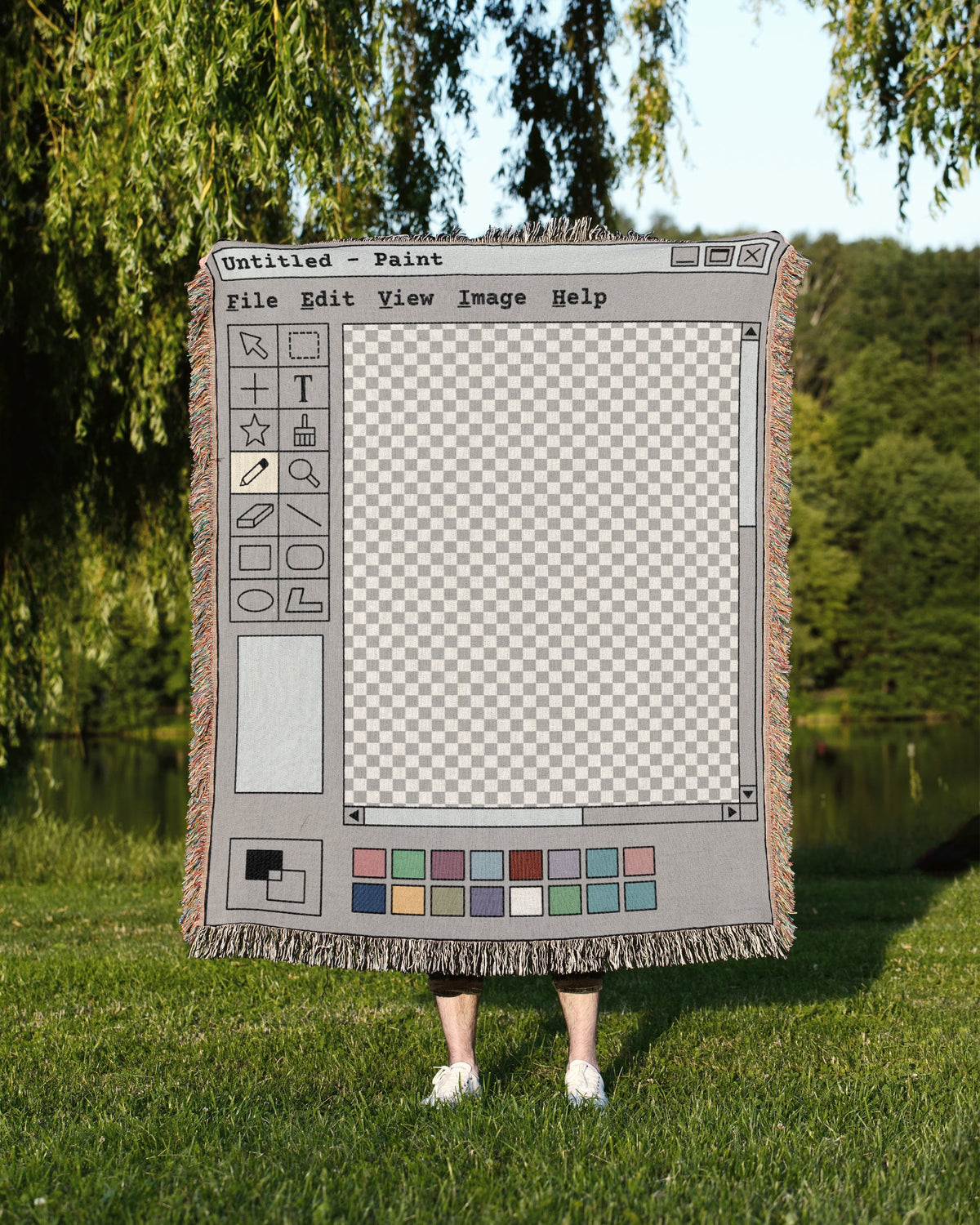 A person standing outdoors on grass in holding up a large woven blanket featuring  a MS Paint 2000s retro computer themed design.